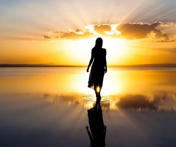 Silhouette of a person walking during a golden sunset over calm water.