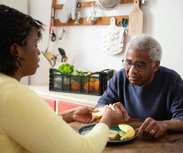 Elderly man and woman sharing a meal and conversation at the kitchen table.