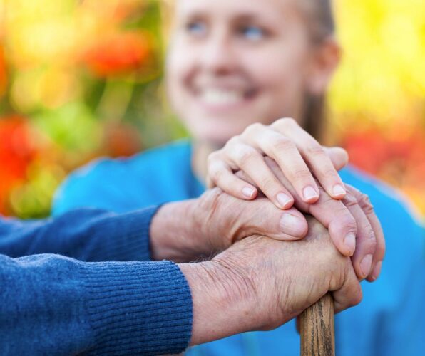 A young woman holding the hand of an elderly person outdoors.