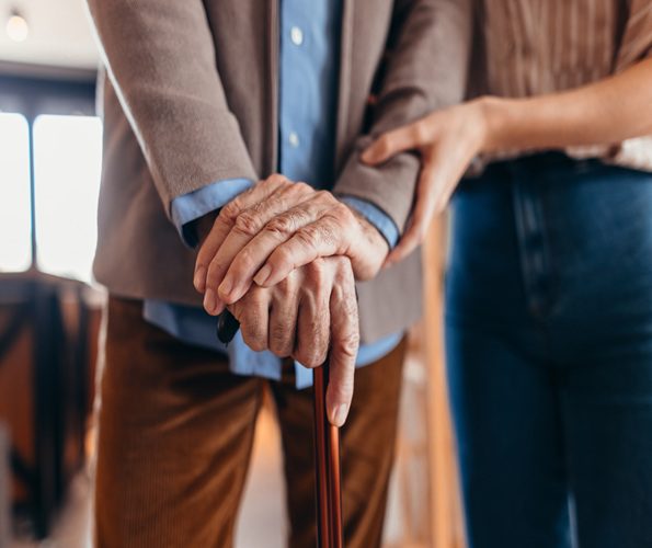 Elderly person with a cane supported by another's hand.