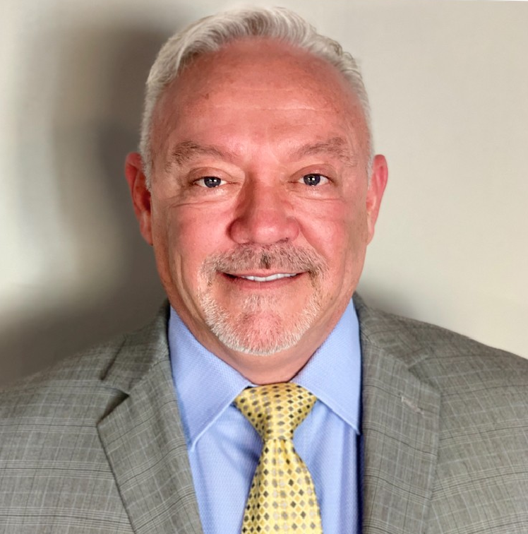 A smiling middle-aged man in a gray suit and yellow tie.