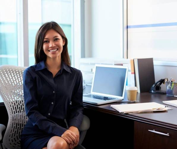 A professional woman smiling while sitting at her office desk.