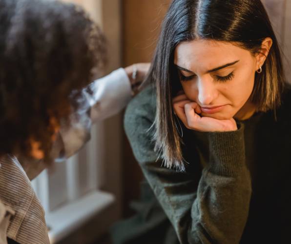 Two women engaged in a serious, empathetic conversation indoors.