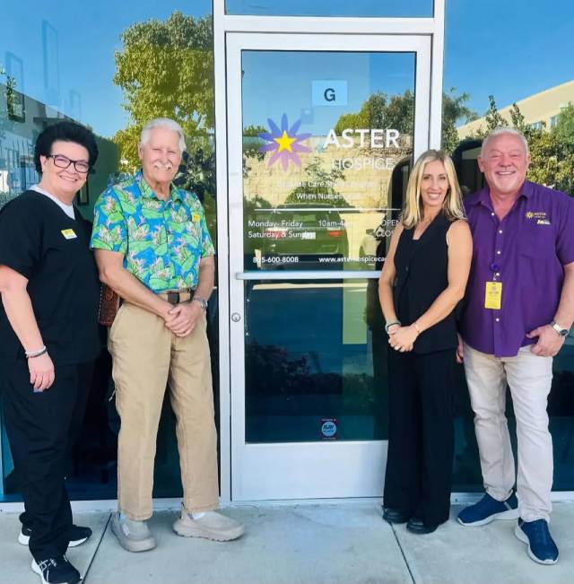Four people standing in front of a glass door with a colorful logo and text.