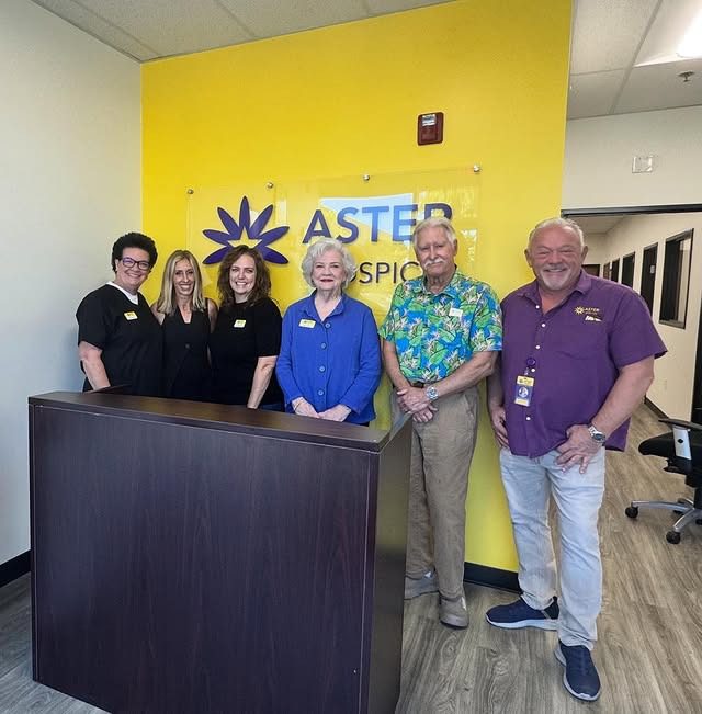 Six people posing behind a reception desk with a yellow wall and logo.